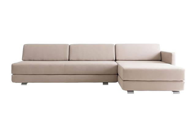 Beige hoekbank met chaise longue rechts, gestoffeerd, moderne vormgeving met grijze poten tegen witte achtergrond.