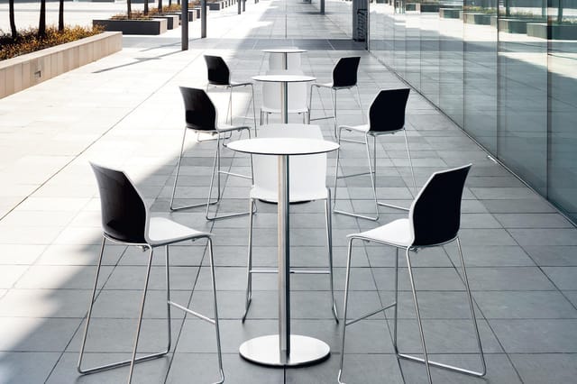 Moderne barkrukken met zwarte zitting en chromen frame rond witte cocktailtafel op terras met grijze tegels.