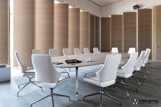 Moderne vergaderruimte met ovale tafel, witte kantoorstoelen op wielen, houten wandpanelen en geïntegreerde verlichting.