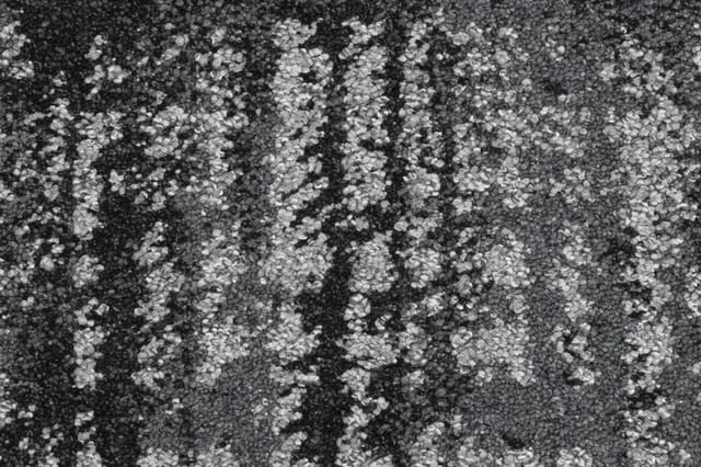 Grijze stof textuur met witte spikkels en donkere verticale strepen, mogelijk tapijt of bekleding materiaal.