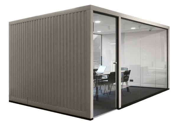 Grijze kantoorbelcel met golfplaat zijwanden, glazen deur en voorzijde. Binnenin bureau met laptop, twee stoelen en verlichti