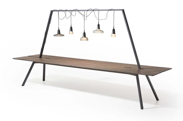 Moderne vergadertafel met zwart metalen frame en houten blad, voorzien van hanglampen boven het tafelblad.