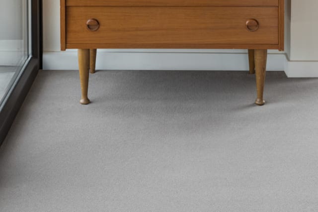 Houten retro dressoir met tapered poten op grijze tapijttegels in moderne kantoorruimte.