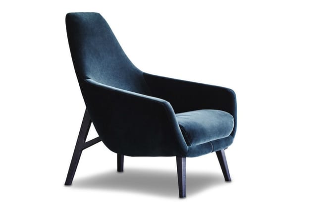 Blauwe fauteuil met hoge rugleuning, fluweelachtig materiaal, zwarte houten poten, modern design, tegen witte achtergrond.
