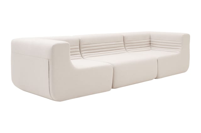 Modulaire bank in lichtbeige stof met afgeronde vormen, opgebouwd uit meerdere blokken, tegen witte achtergrond.