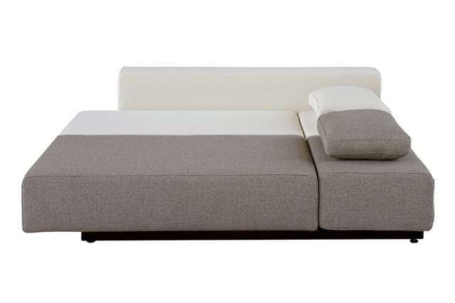 Modulaire loungebank in grijsbeige stof met crèmekleurig rugkussen en bijzettafel op zwart onderstel.