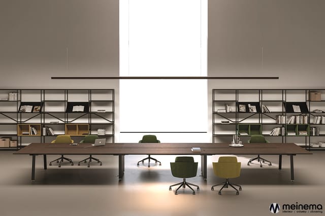 Modern kantoor met lange houten vergadertafel, groene en gele bureaui stoelen, metalen kasten met boeken aan weerszijden, gro