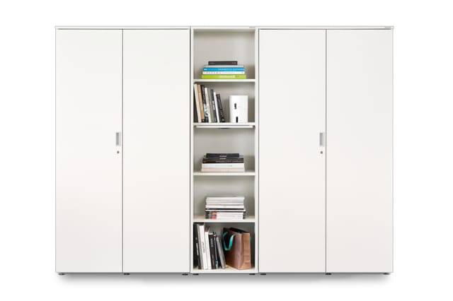 Witte schuifkastenwand met centrale open boekenkast, gevuld met boeken en kantooraccessoires.