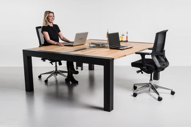 Houten vergadertafel met zwart onderstel, zwarte bureaustoelen met netrug, laptops en kantoorartikelen op het tafelblad in mo