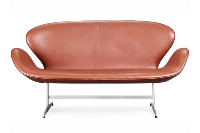 Roodbruine moderne sofa met gebogen armleuningen en metalen U-vormig onderstel op witte achtergrond.