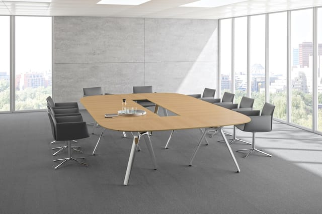 Moderne vergaderruimte met ovale houten vergadertafel, witte onderstel, grijze stoelen, betonnen wand, grote ramen met uitzic