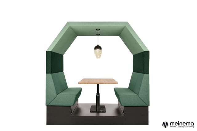 Groene akoestische belcel met twee zitplaatsen, houten tafel, hangende glazen lamp en donker onderstel.