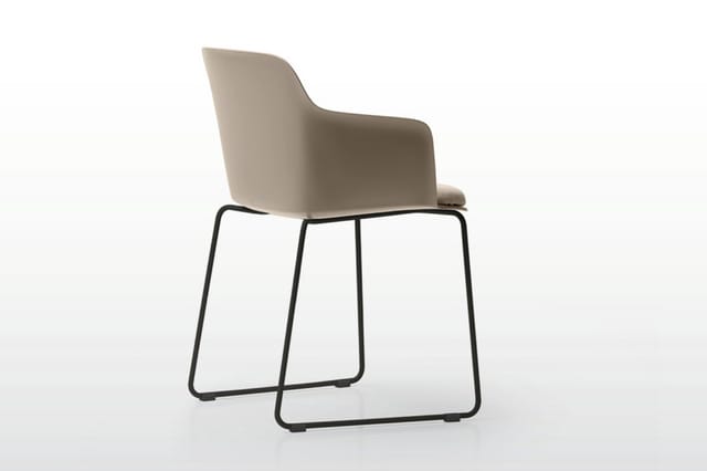 Beige stoel met armleuningen en zwart metalen sledes onderstel, tegen witte achtergrond.