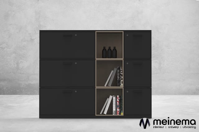 Zwarte kastenwand met drie open vakken in het midden, gevuld met boeken en flessen. Tegen grijze betonnen achtergrond.