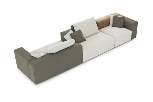 Lange modulaire bank in grijstinten en crème met meerdere zitplekken, decoratieve kussens en armleuningen, schuin aanzicht.