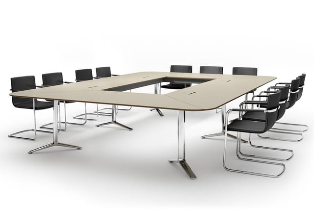 U-vormige vergadertafel in licht hout met chrome onderstel, omringd door zwarte kantoorstolen met chroom frame op witte achte