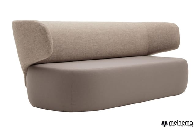 Moderne bank met gebogen vormen, grijs-beige bekleding, cilindervormige rugkussen, zitgedeelte met afgeronde vormen.