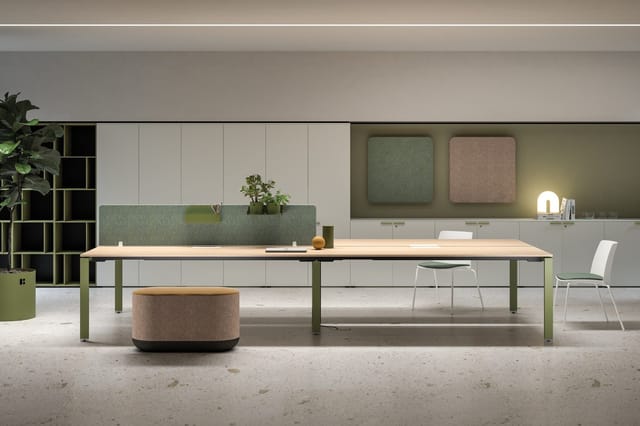Modern kantoor met lange houten tafel op groene poten, ronde zitpoef in beige, groene akoestische schermen, witte kastensyste