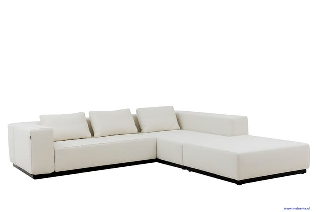 Witte hoekbank met chaise longue, minimalistisch design, zwarte voetlijst, drie losse kussens op de rugleuning.