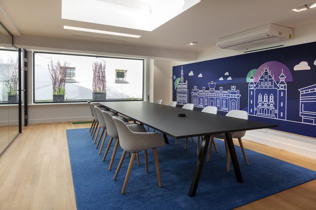 Moderne vergaderruimte met zwarte vergadertafel, grijze stoelen, blauwe rug, raam met uitzicht, skyline muurschildering op do