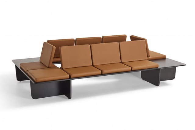 Lange bruinleren bank met zwart metalen onderstel en grijs werkblad, vier zitplaatsen met ergonomische rugleuningen.