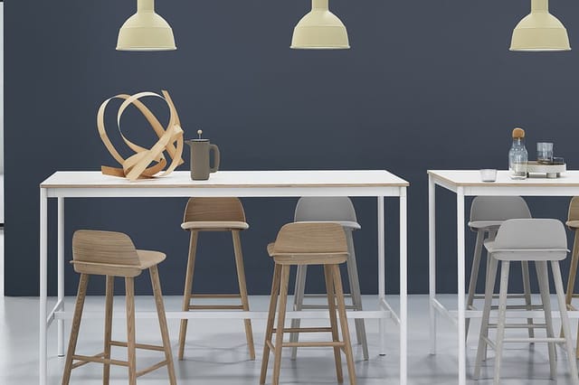 Kantoor eetkeuken met witte tafels, houten en grijze barstoelen, donkerblauwe wand, drie goudkleurige hanglamps en decoratiev