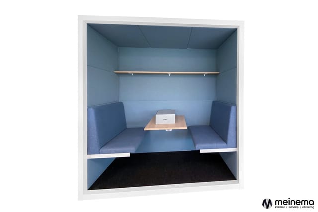 Blauwe belcel met zitbanken aan weerszijden, houten tafel met laptop, wandplank en zwarte mat op vloer.