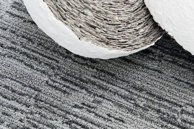 Gerolde grijze en witte akoestische stof tegen textielachtergrond met grafische streeppatroon.