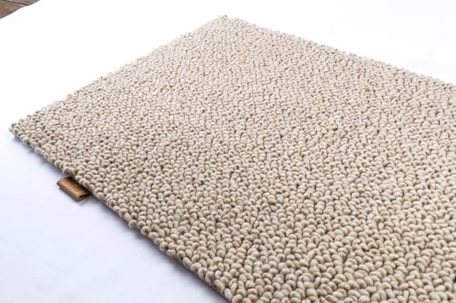 Beige gestructureerde tapijttegel met dichte, gebobbelde wolvezels op witte ondergrond.