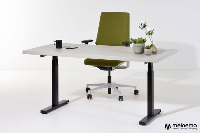 Wit elektrisch verstelbaar bureau met zwarte onderstel en groene bureaustoel, ingericht met koffiemok, plant en bloemen.
