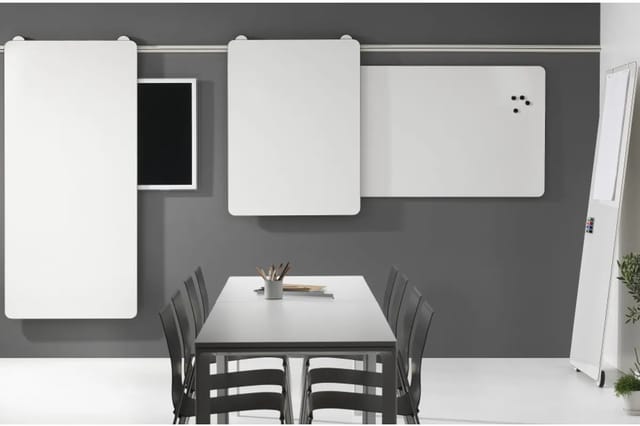Vergaderruimte met grijze wanden, witte whiteboarden, zwarte stoelen rond tafel, flipchart en kantoormaterialen.