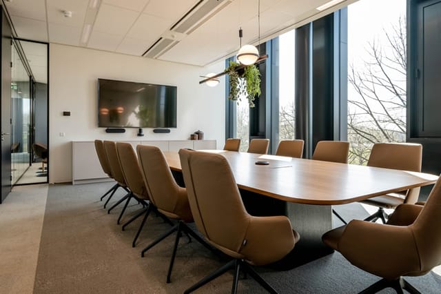 Moderne vergaderruimte met wit blad tafel, bruine draaistoelen, wandmontage TV, hangende groene planten en grote ramen met ui