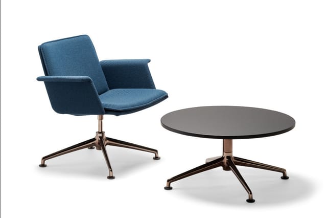 Blauwe kantoorstoel met armleuningen en ronde grijze tafel op wielbasis, beide met bronzen poten.