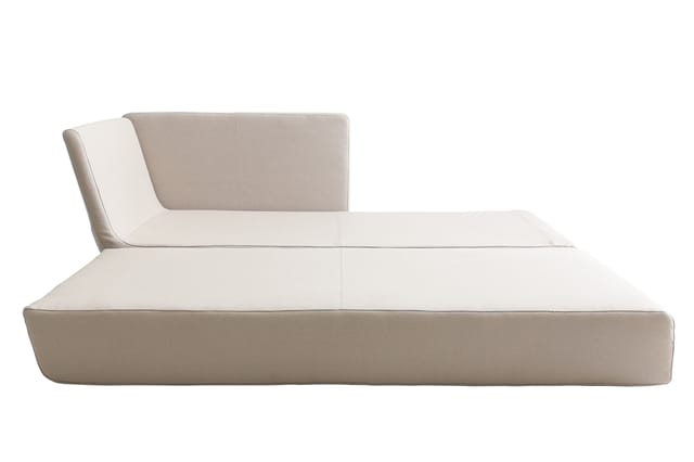 Beige loungebank met lage zitting, hoge rugleuning en zijkussen tegen witte achtergrond.