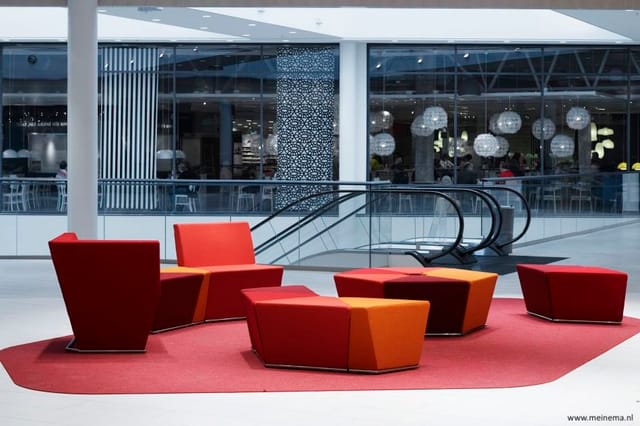 Rode en oranje modulaire zitgroep op roze tapijt in modern interieur met glazen wand en trap op achtergrond.