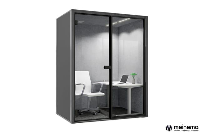 Gesloten belcel met glazen deuren en zwart frame, grijze akoestische wanden, wit bureau, bureaustoel en laptop, groene plant.