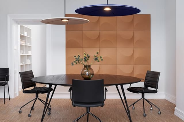 Moderne vergaderkamer met ronde zwarte tafel, vier zwarte stoelen met wielen, bruine 3D wandpanelen, houten vloer, twee hange