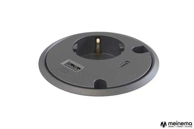 Grijs rond bureau-inbouw element met centraal stopcontact, USB-poort en kabelgat, bovenaanzicht.