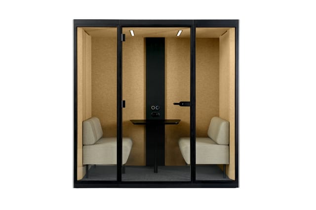 Akoestische belcel met zwart frame, beige wanden, grijze vloer, twee beige stoelen, zwarte tabel met monitorarm en verlichtin