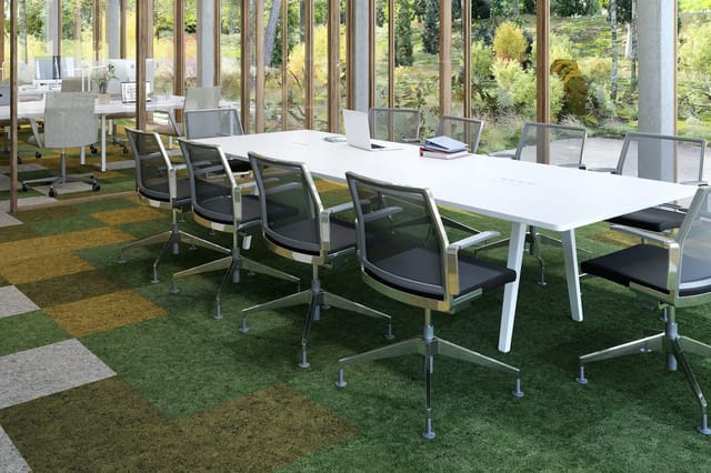 Moderne vergaderzaal met witte rechthoekige tafel, zwarte ergonomische stoelen met wielen, groen tapijt, grote glazen wand me