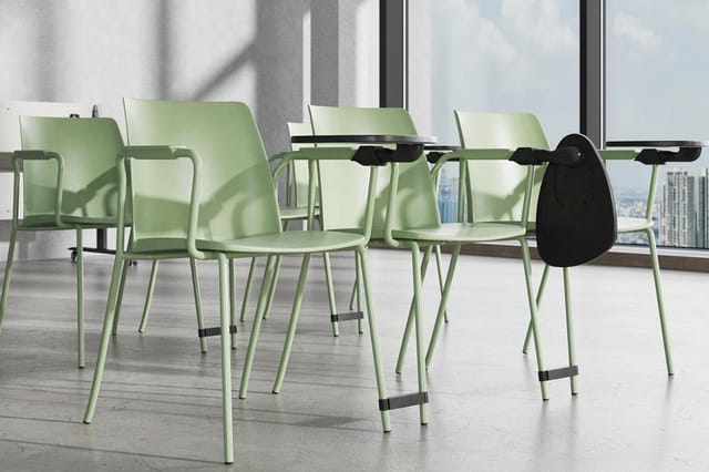 Groene stapelstoelen met armleuningen en zwarte details rond een vergadertafel in modern kantoor met grote ramen en stadsuitz