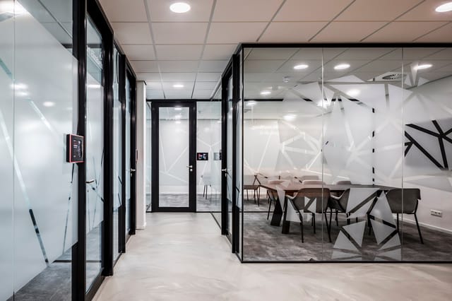 Kantoorgang met zwarte glazen afscheidingen, witte frosted glass deuren, grijze vloer en moderne plafondverlichting. Zicht op