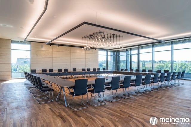 Moderne vergaderzaal met lange houten tafel, zwarte kantelstoelen, houten vloer, betonnen wanden en glazen wanden met uitzich