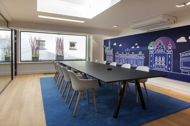 Moderne vergaderruimte met zwarte rechthoekige tafel, grijze stoelen, blauwe vloerkleed, grote ramen, skyline-muurschildering