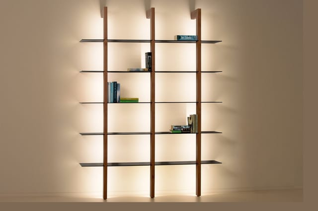 Modulair kastensysteem met drie houten verticale delen en zes zwarte horizontale legplanken, gevuld met boeken. Indirecte ach