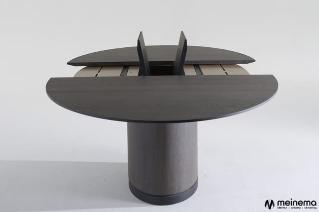 Ronde vergadertafel met grijze houten blad en zuilvormige onderstel, uitschuifmechanisme zichtbaar aan bovenkant.