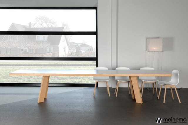 Moderne vergaderruimte met lange houten tafel, witte stoelen en grote raampartijen met uitzicht op landelijk gebied.