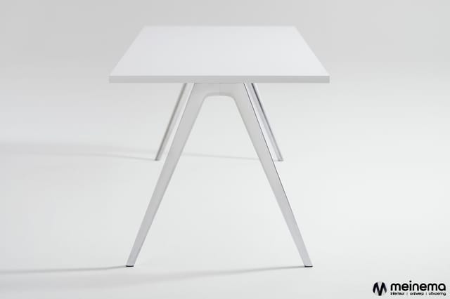 Witte trapeziumvormige vergadertafel met schuine aluminium poten op grijze achtergrond.
